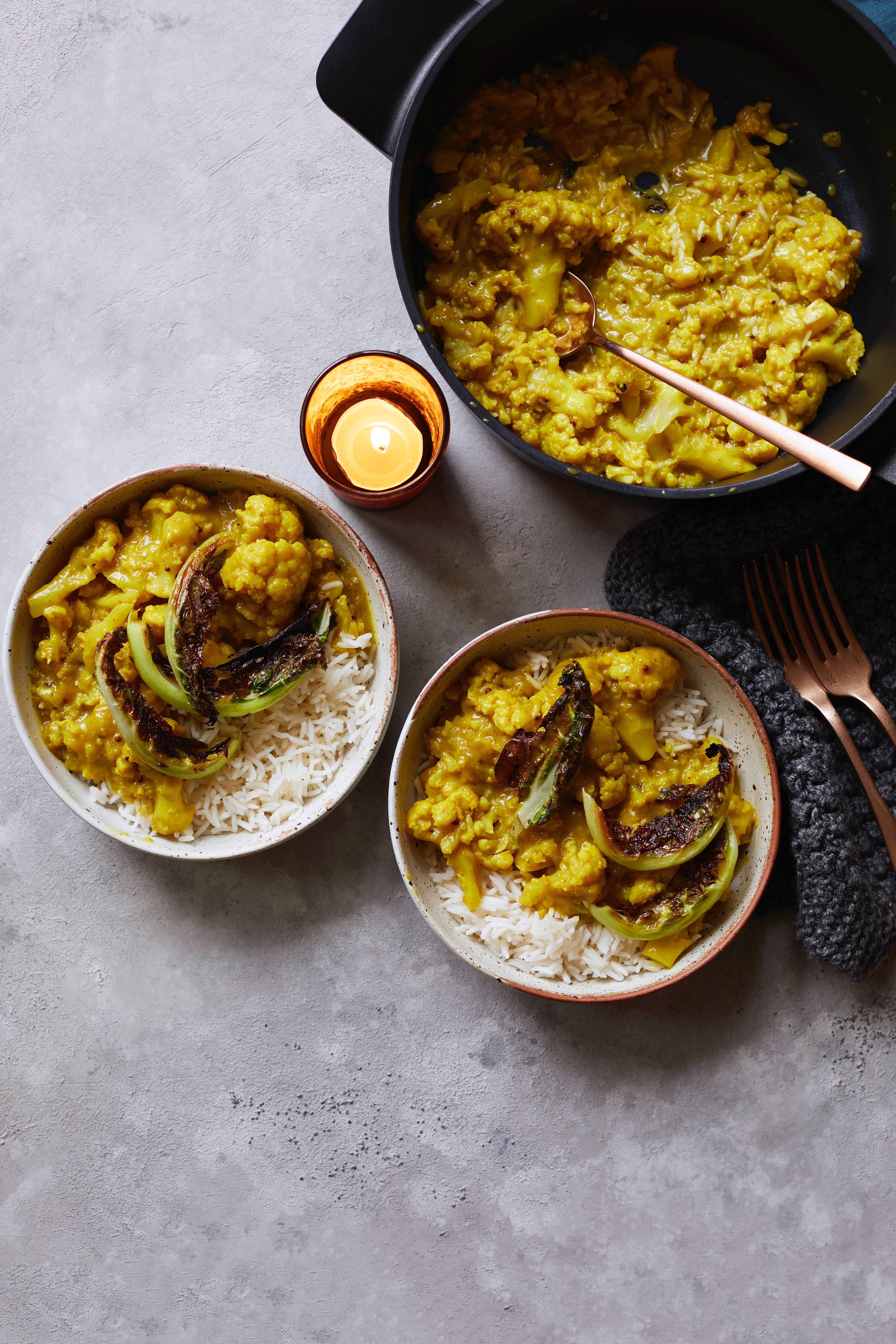 Două boluri de conopidă curry cu orez, așezate una lângă cealaltă cu un set de tacâmuri în dreapta