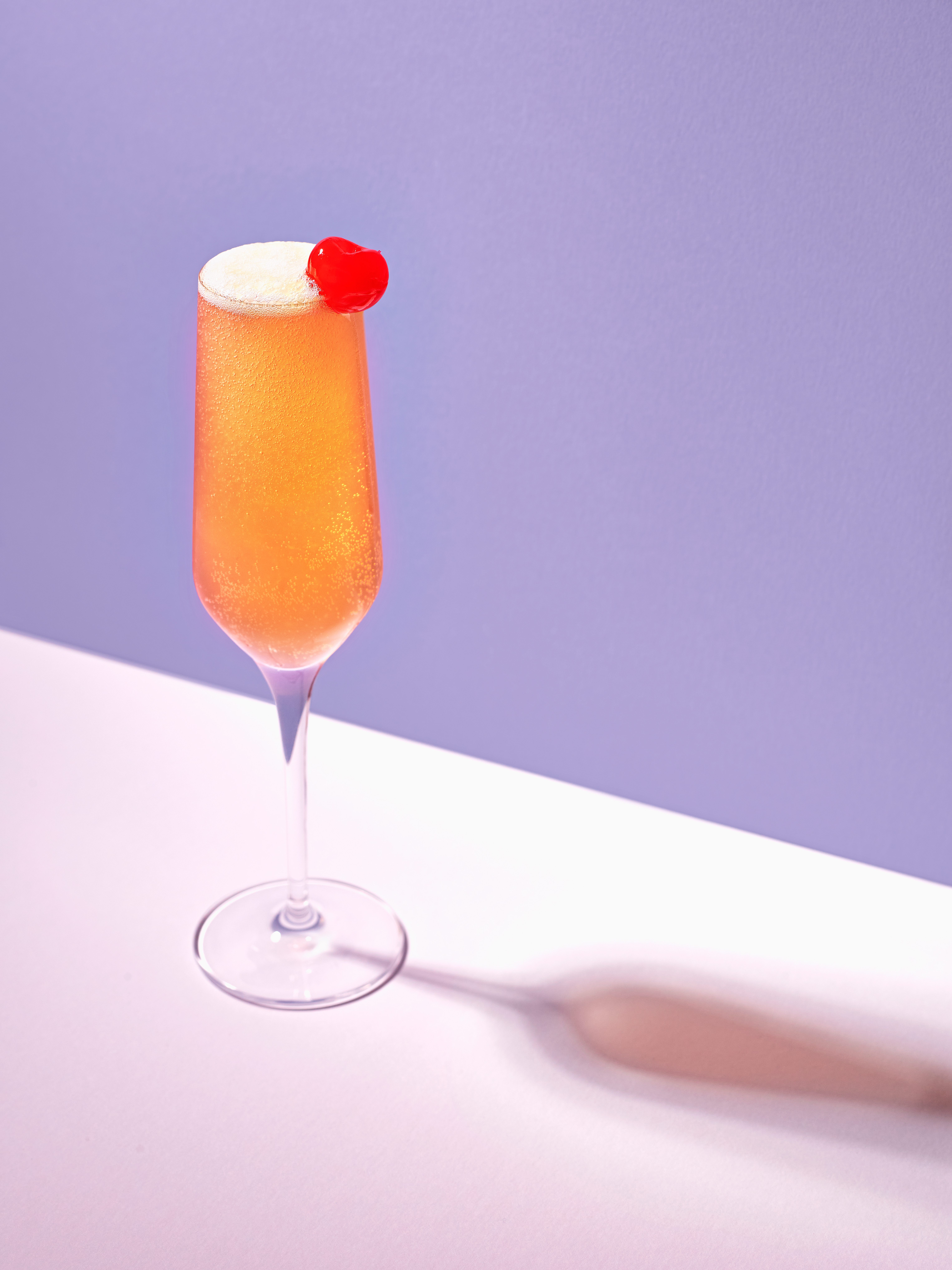Un pahar lung și îngust umplut cu un cocktail de portocale cu o cireșă maraschino pe partea laterală a paharului