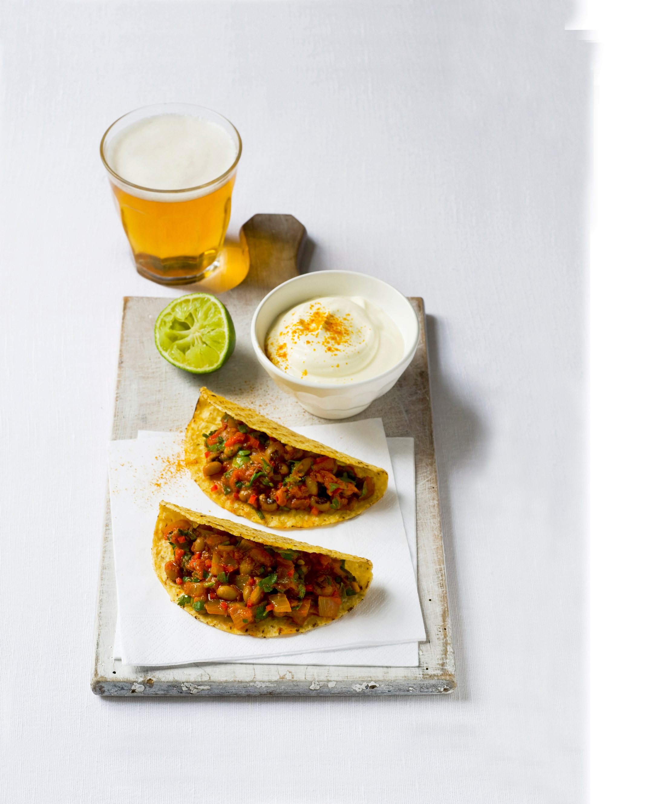 Tacos cu ardei iute, o oală de smântână și felie de lime pe o placă albă
